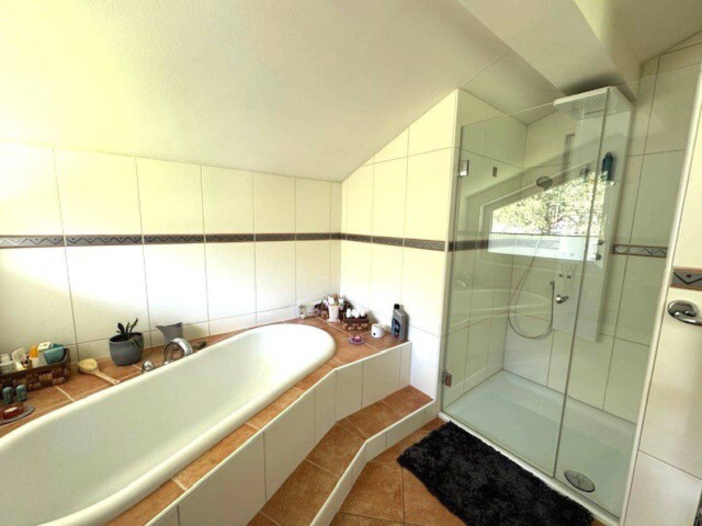 Badezimmer mit Badewanne, moderner Glasdusche, Fliesenboden und Dachschräge.