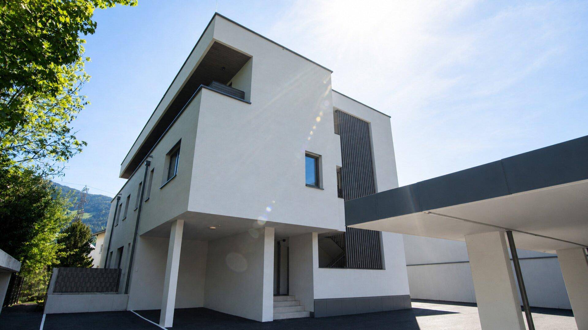 Modernes Wohngebäude mit Carport und klaren architektonischen Elementen unter strahlendem Himmel.
