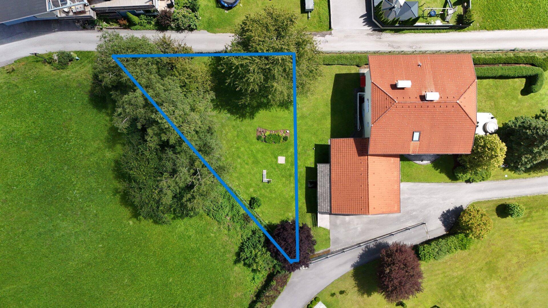 Luftaufnahme des Grundstücks mit blau umrandeter Fläche, umgeben von Grünflächen und Bäumen.