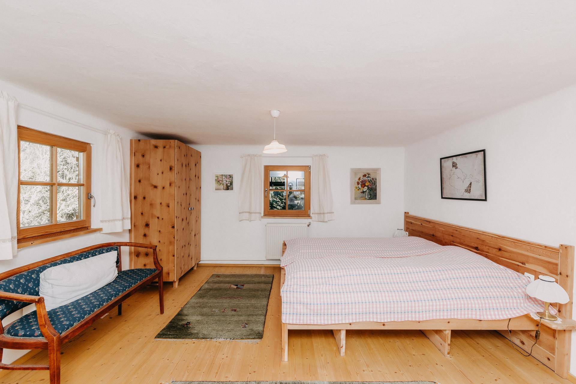 Helles Schlafzimmer mit Doppelbett, Holzschrank und traditioneller Sitzbank.