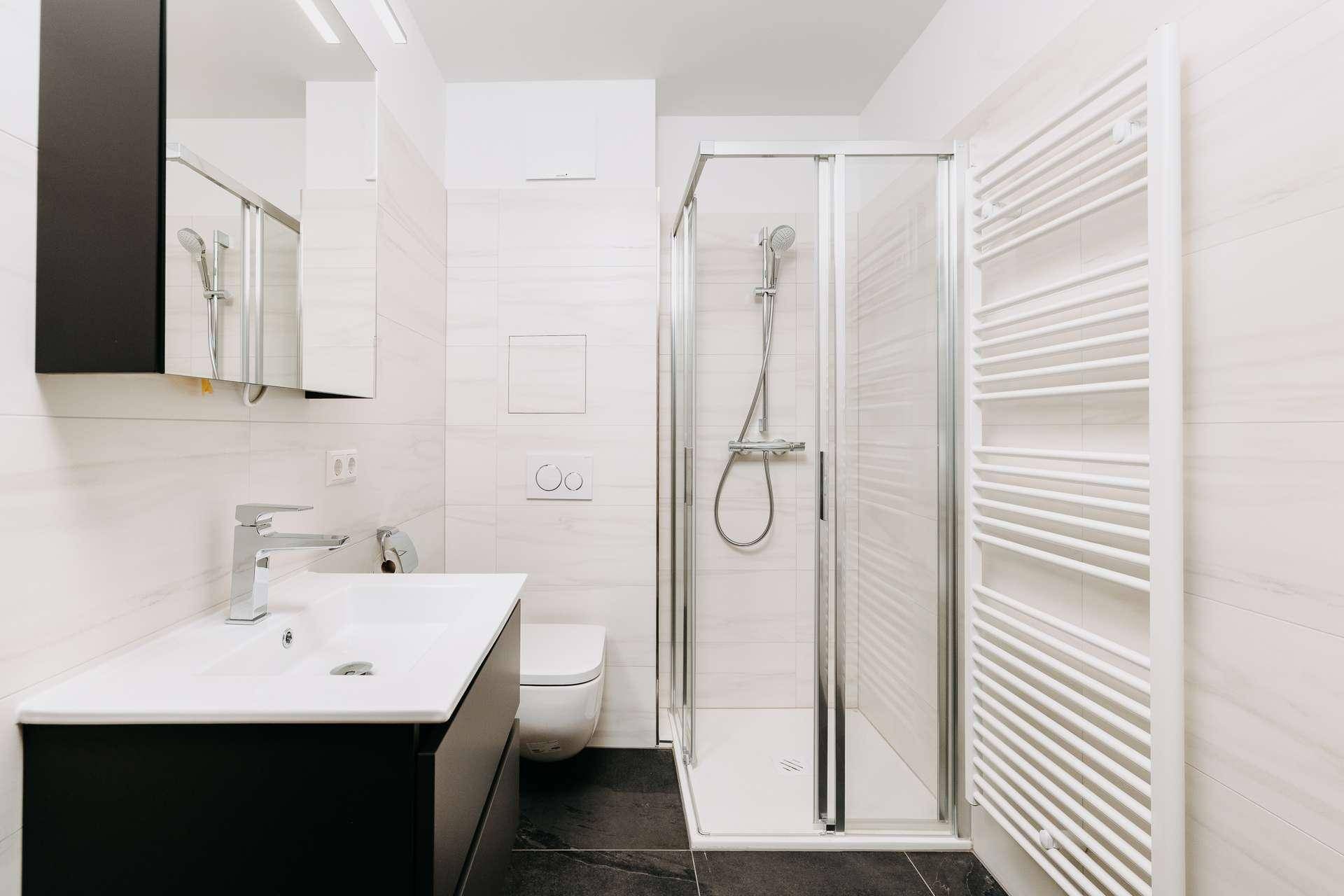 Modernes Badezimmer mit Duschkabine, Waschtisch, Toilette und beheiztem Handtuchhalter.