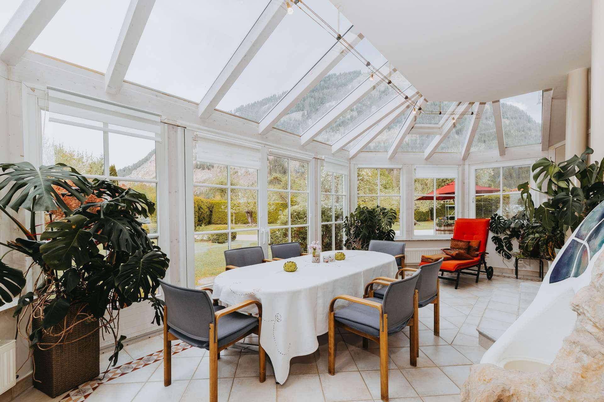 Geräumiger Wintergarten mit Glasdach, Esstisch und Panoramablick auf die Berge und den Garten.