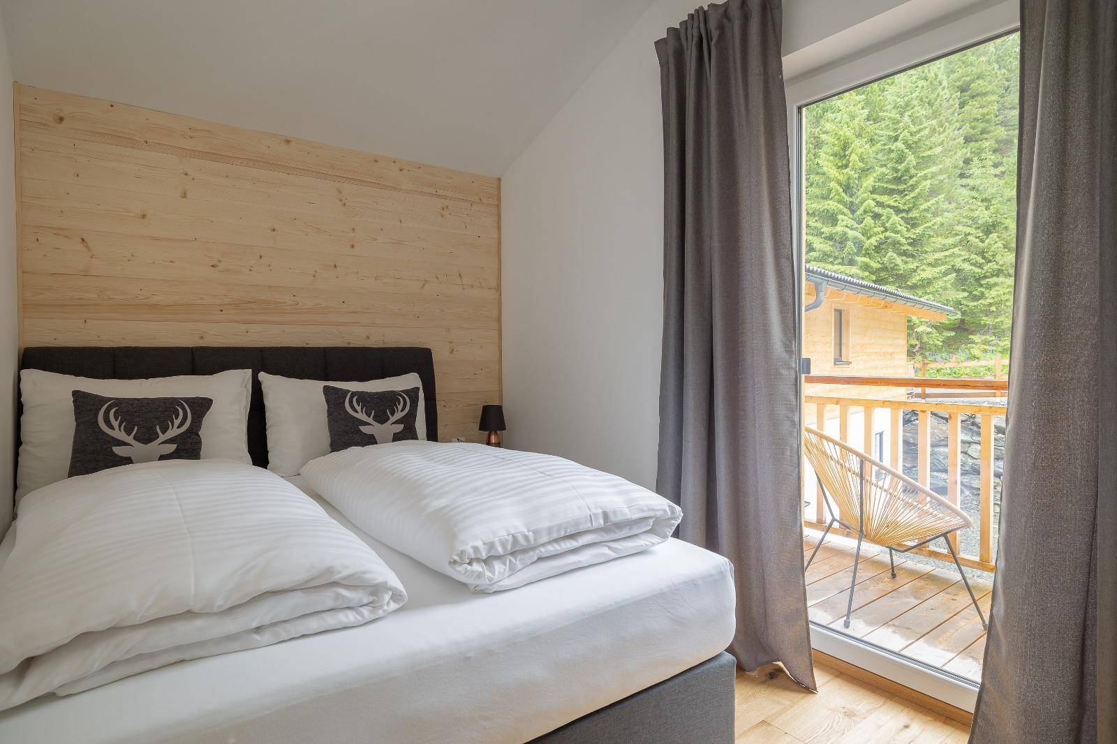 Gemütliches Schlafzimmer mit Holzwand, Doppelbett und Zugang zum Balkon.
