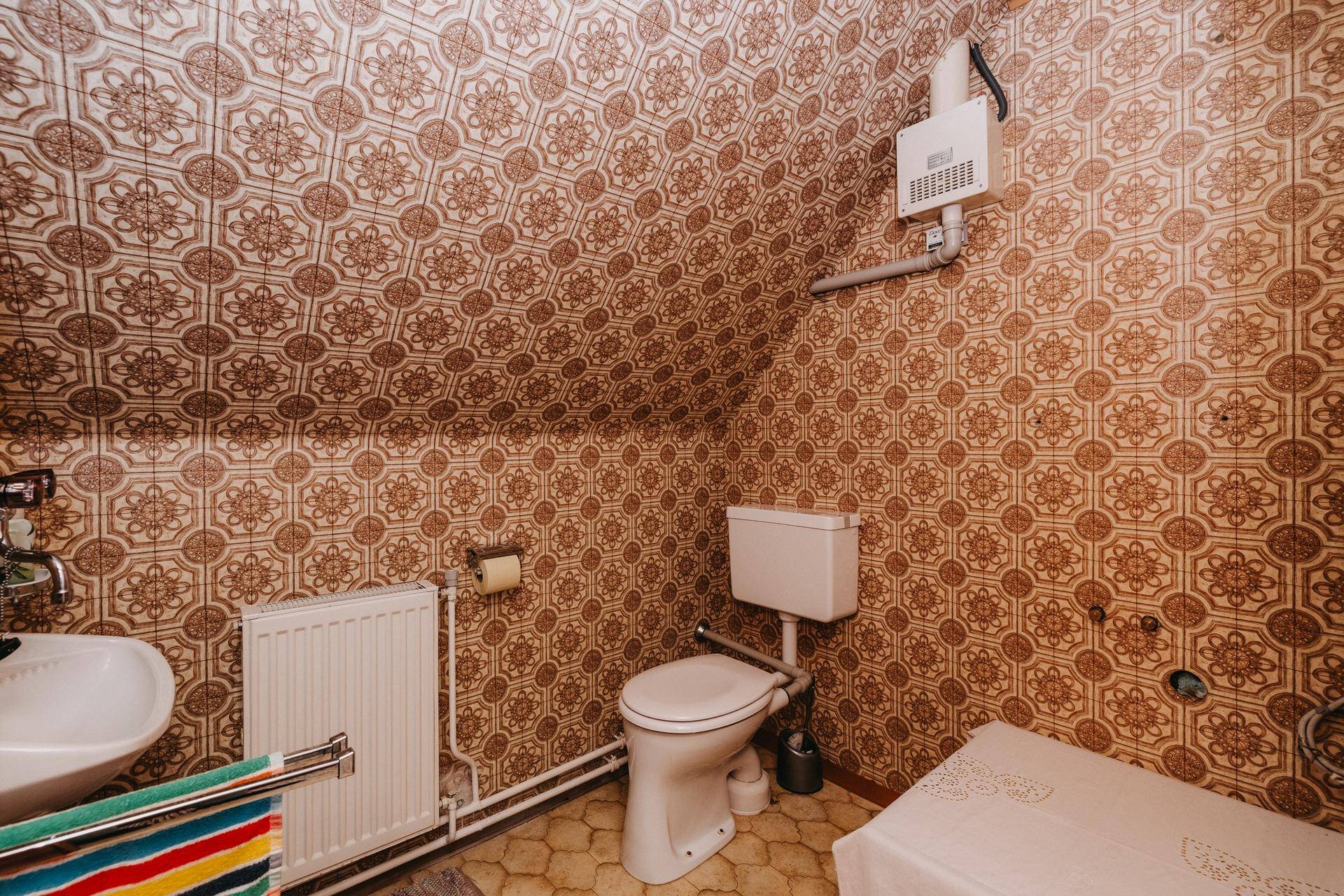 Kleines WC im Dachgeschoss mit gemusterter Tapete und einfacher Ausstattung.