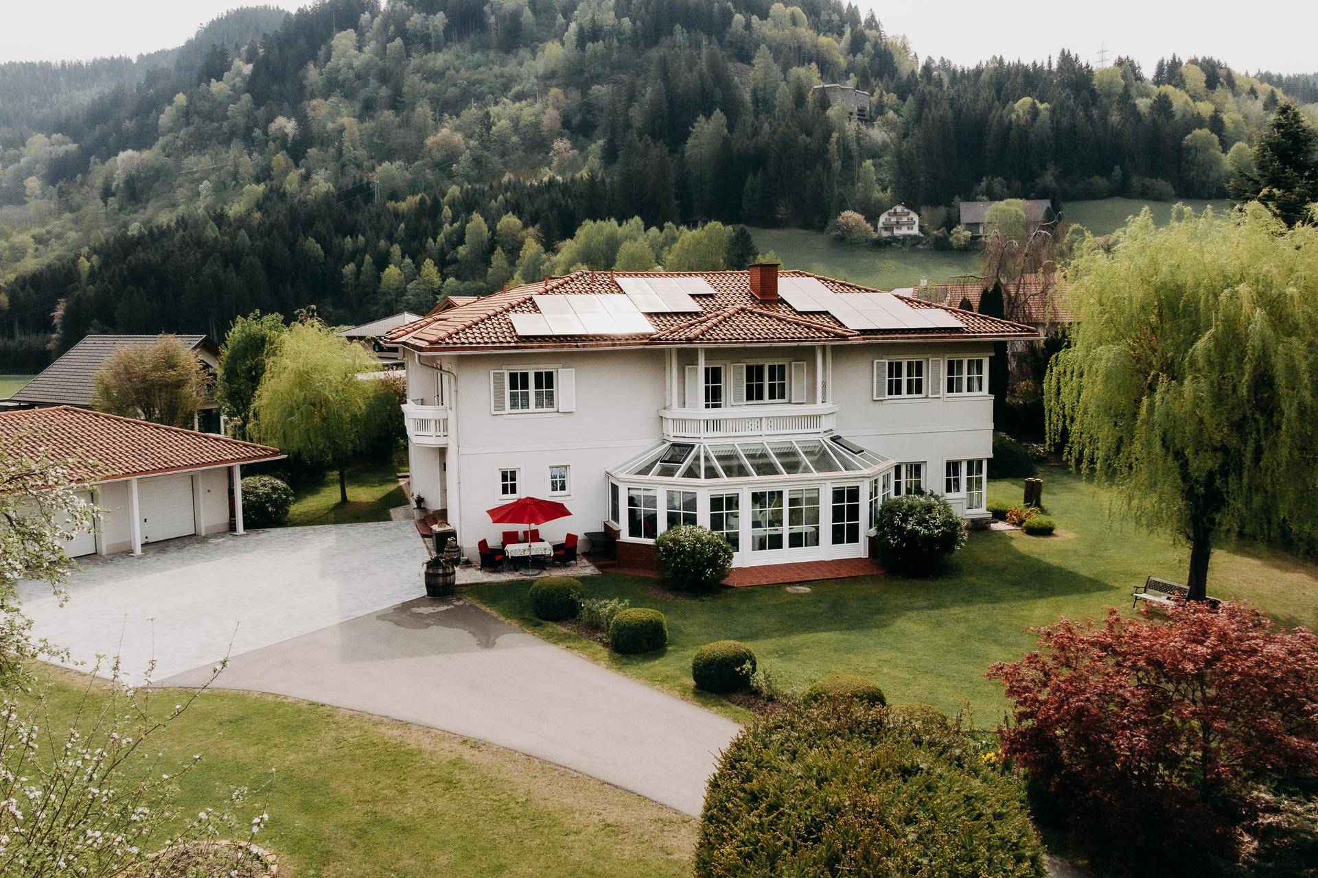 Ansicht des Hauses mit Photovoltaikanlage auf dem Dach, Wintergarten und gepflegtem Gartenbereich.