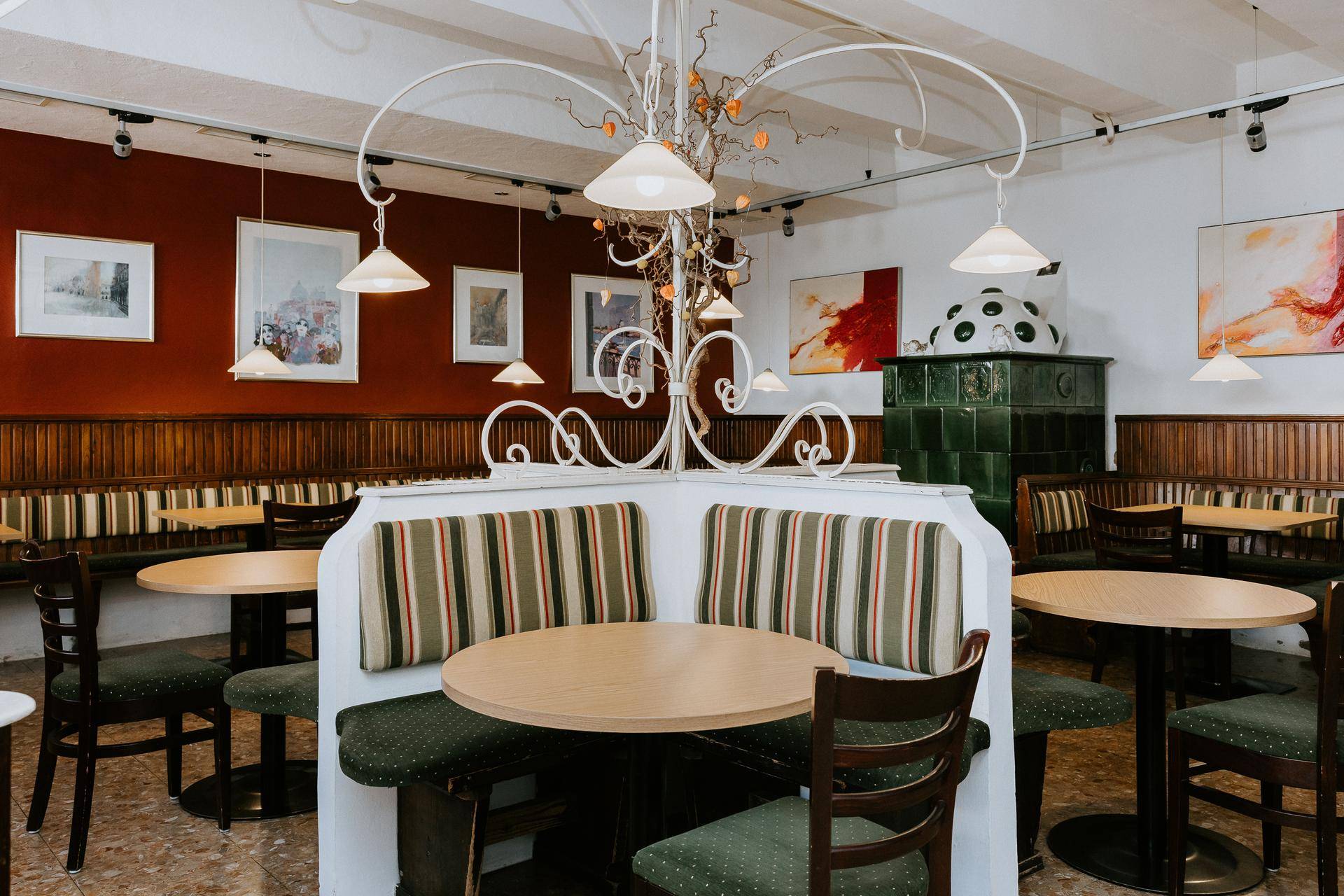 Restaurantinterieur mit traditionellem Kachelofen, Holzbänken und runden Tischen.