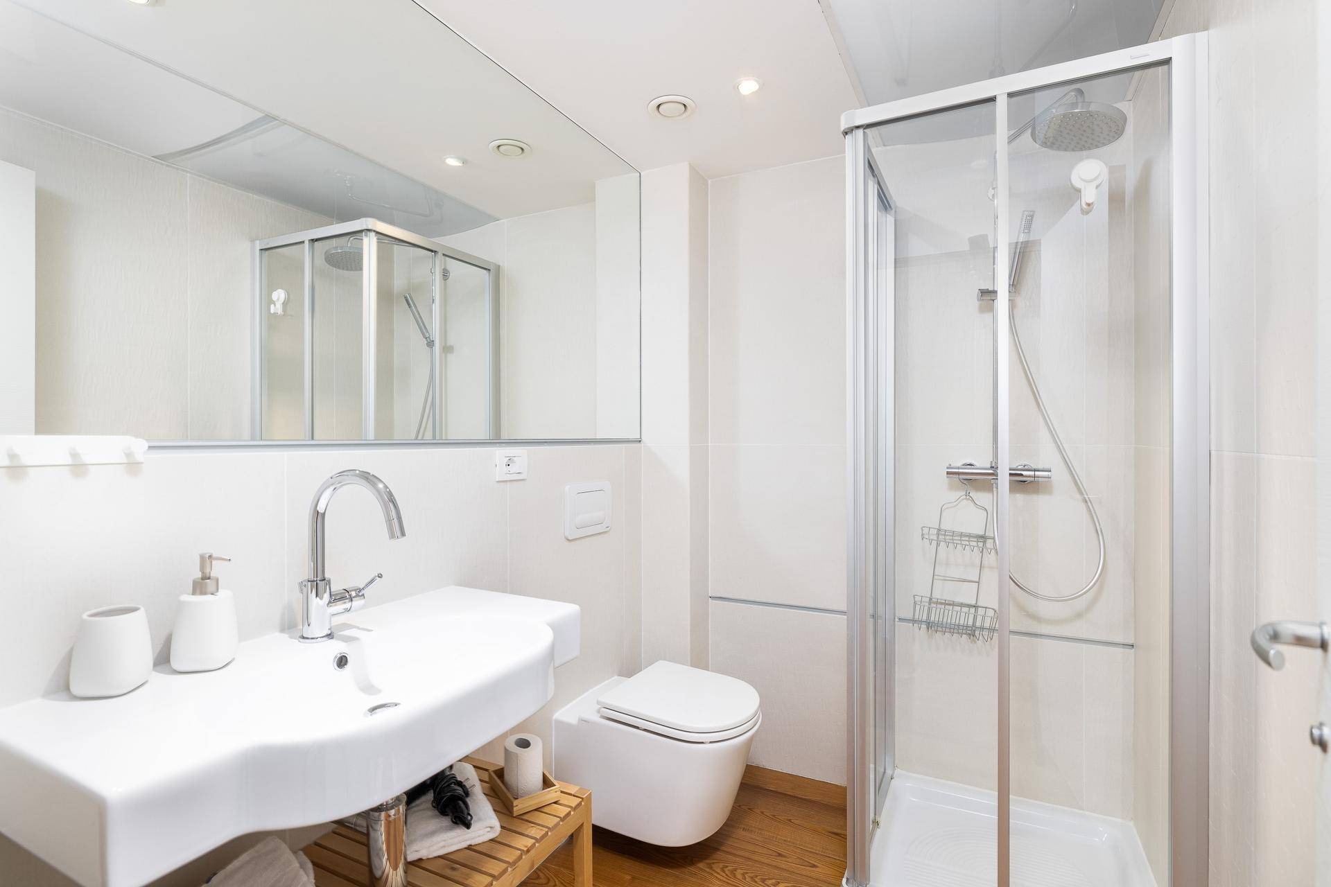 Modernes Badezimmer mit weißen Fliesen, Einzelwaschbecken, WC und einer Duschkabine mit Spiegel.