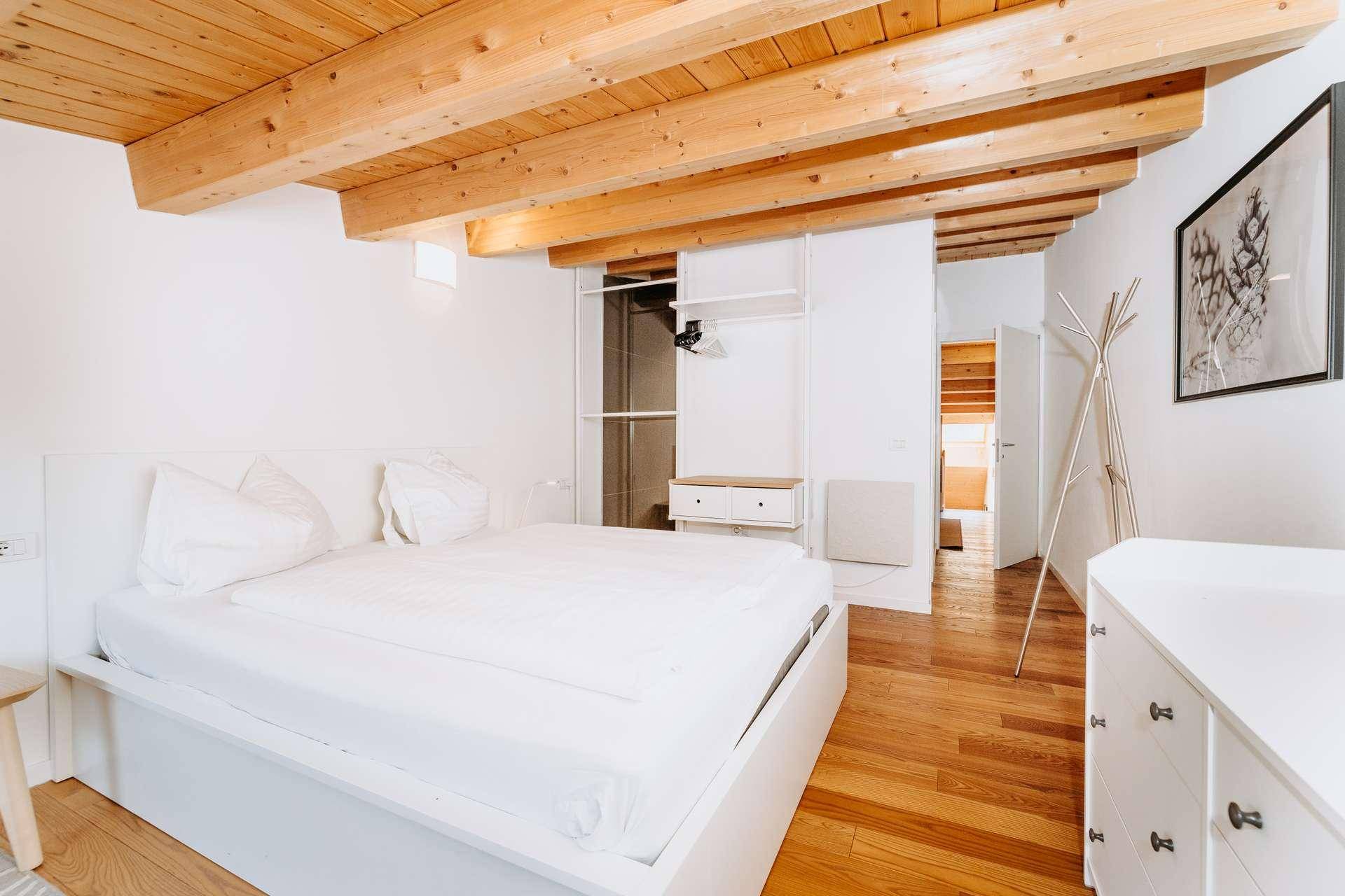 Schlafzimmer mit Holzbalkendecke, Holzboden und offenem Kleiderschrank.