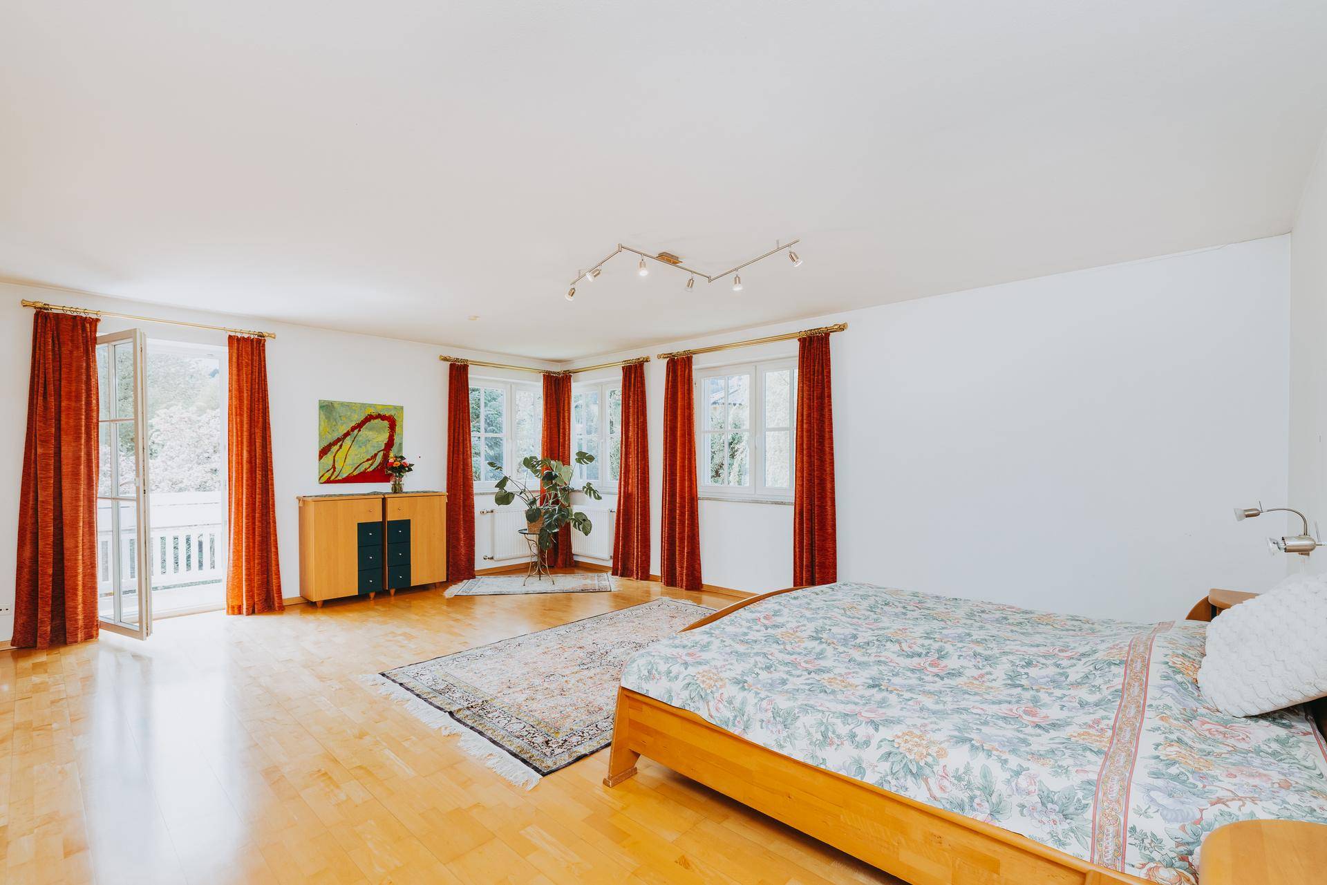 Geräumiges Schlafzimmer mit Holzbett, Parkettboden und Zugang zu einem Balkon.