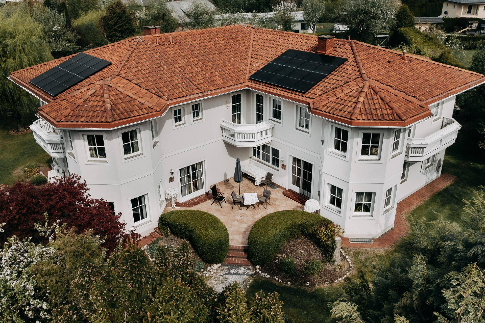 Rückseite des Hauses mit einer gefliesten Terrasse, Gartenmöbeln und Photovoltaikanlage auf dem Dach.