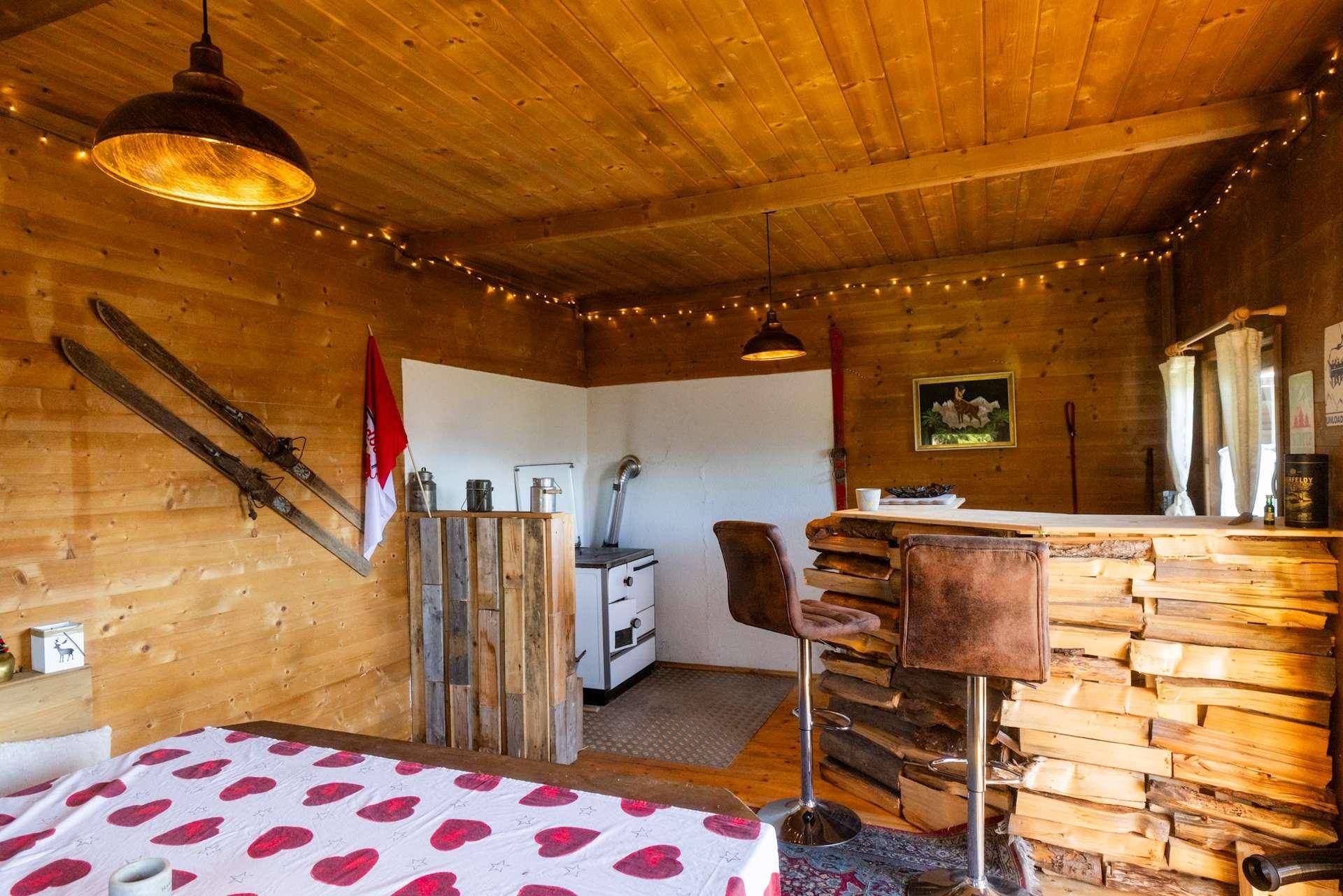 Rustikaler Essbereich mit einer Holzbar, einem Kaminofen und traditioneller Dekoration in einer Holzhütte.