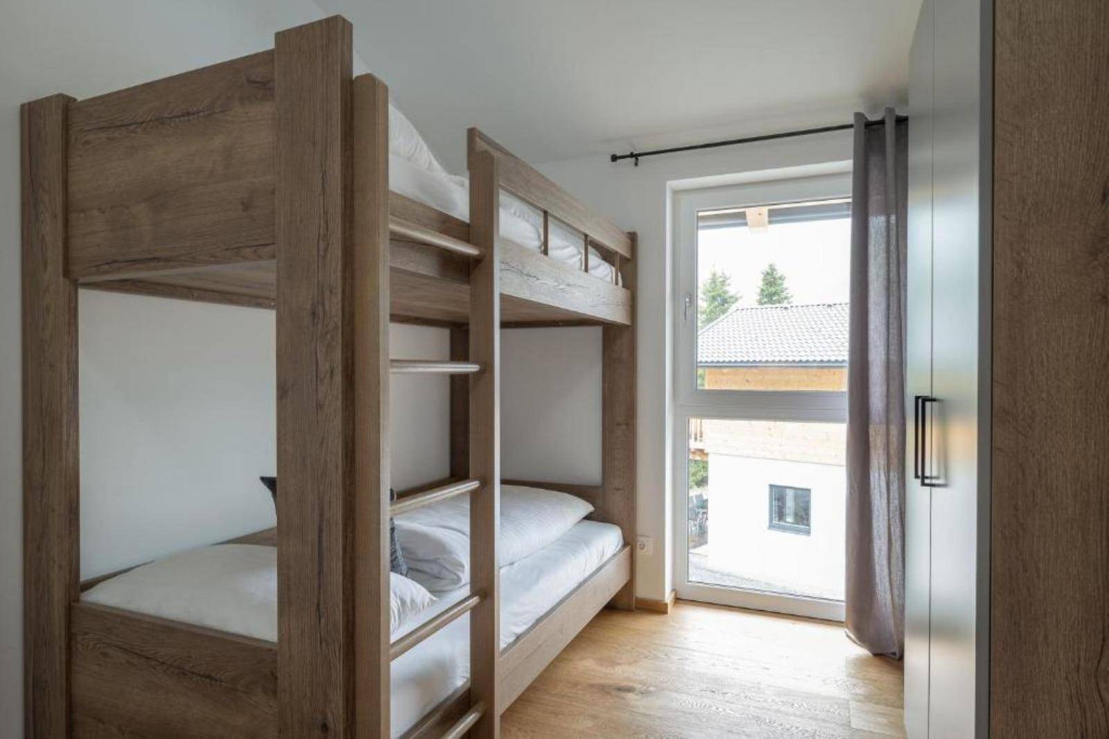 Kinderzimmer mit Etagenbett, Holzboden und Fenster mit Blick nach draußen.