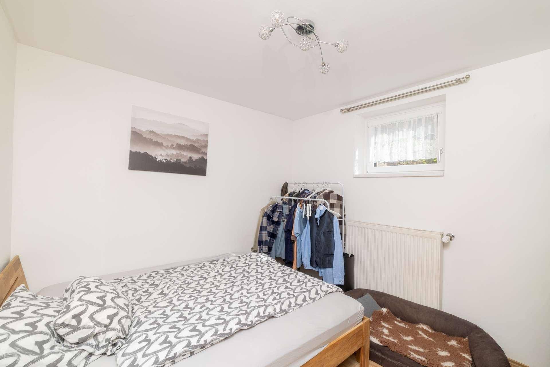 Einfaches Schlafzimmer mit Einzelbett, Kleiderstange und kleinem Fenster.