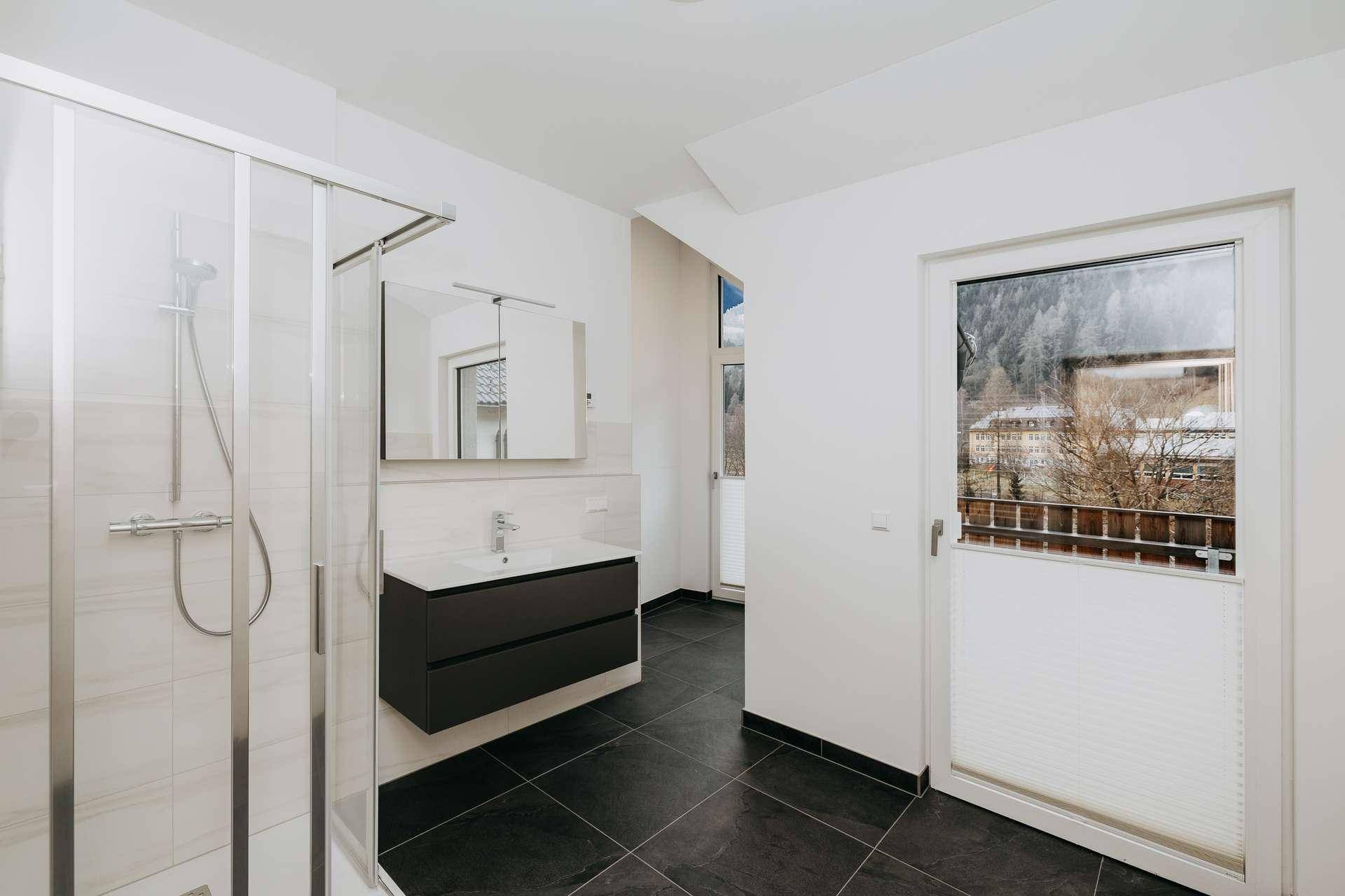 Modernes Badezimmer mit Duschkabine, Einzelwaschbecken und großem Fenster mit Blick ins Grüne.