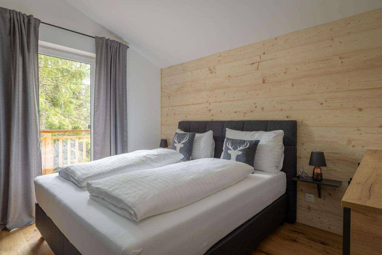 Helles Schlafzimmer mit Holzboden, Holzwand und großem Fenster mit Zugang zum Balkon.