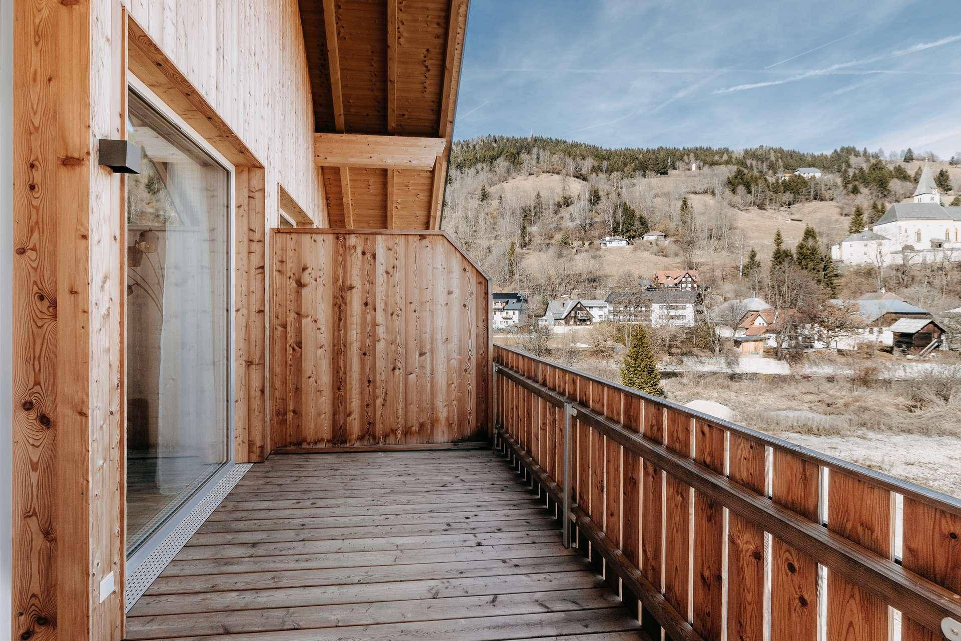 Geräumiger Holzbalkon mit Panoramablick auf die alpine Landschaft und die Nachbarschaft.