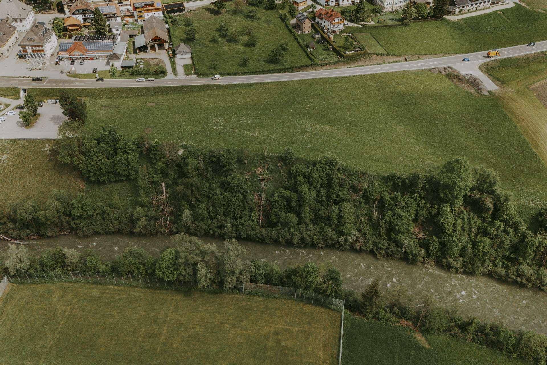 Nahaufnahme aus der Luft eines Flusses, der sich durch eine grüne Landschaft schlängelt, gesäumt von Bäumen und Feldern.