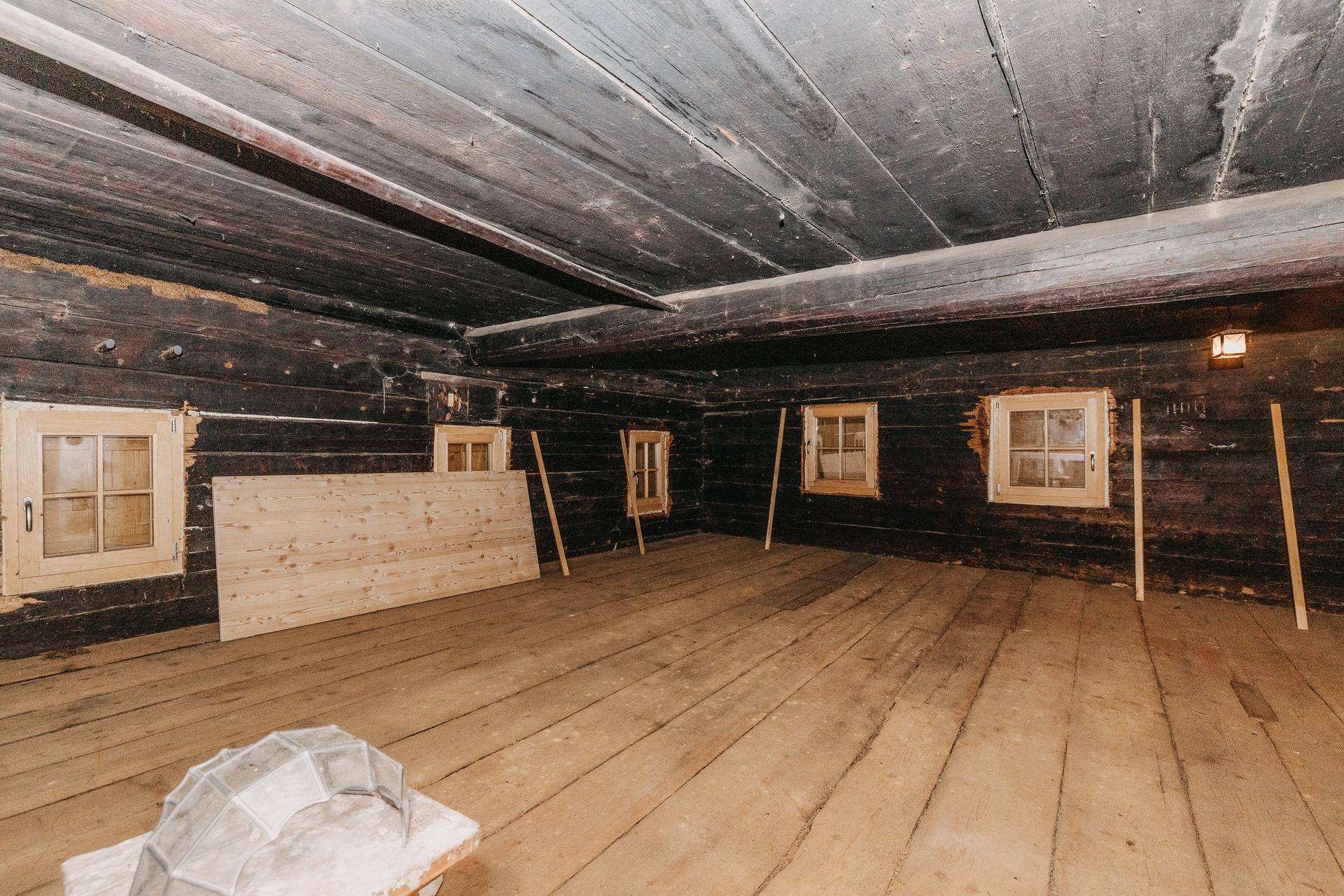 Großer, unfertiger Raum mit dunklen Holzwänden und Holzboden, bereit für den Ausbau.