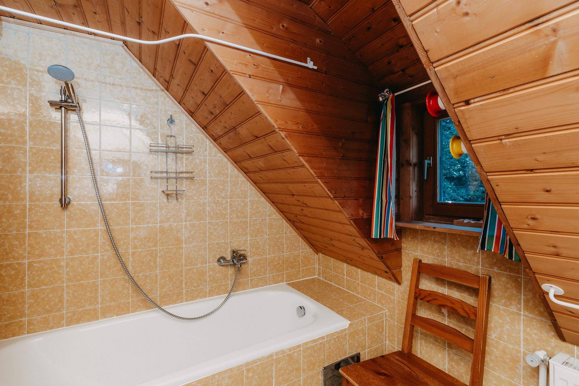 Badezimmer im Dachgeschoss mit Badewanne, Holzverkleidung und schrägen Wänden.
