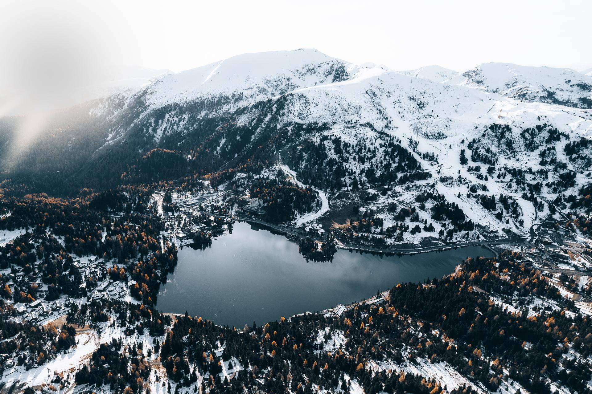 Weitläufige Winterlandschaft mit einem ruhigen See, umgeben von schneebedeckten Bergen und Nadelbäumen.