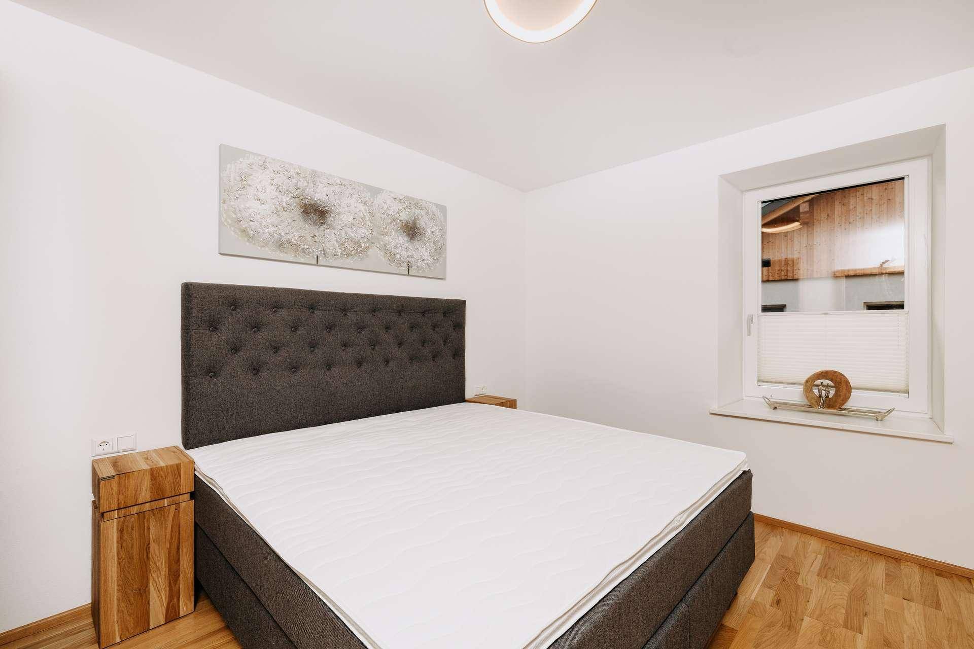 Helles Schlafzimmer mit großem Doppelbett, Holzboden und Fenster für natürliches Licht.