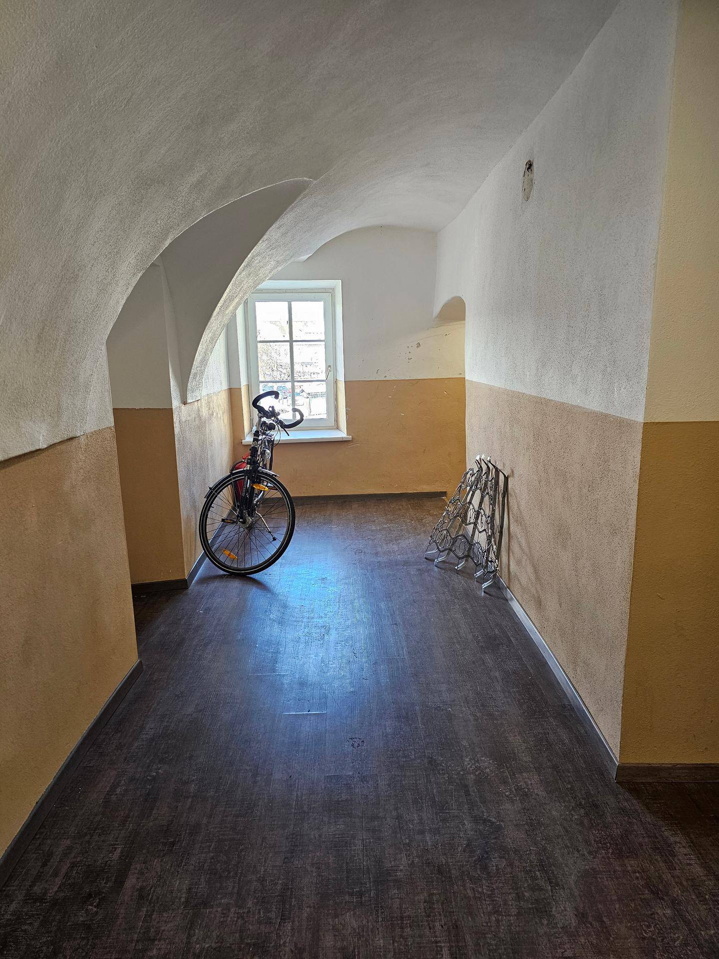 Gewölbter Flur mit dunklem Laminatboden und einem Fenster, das Tageslicht hereinlässt.