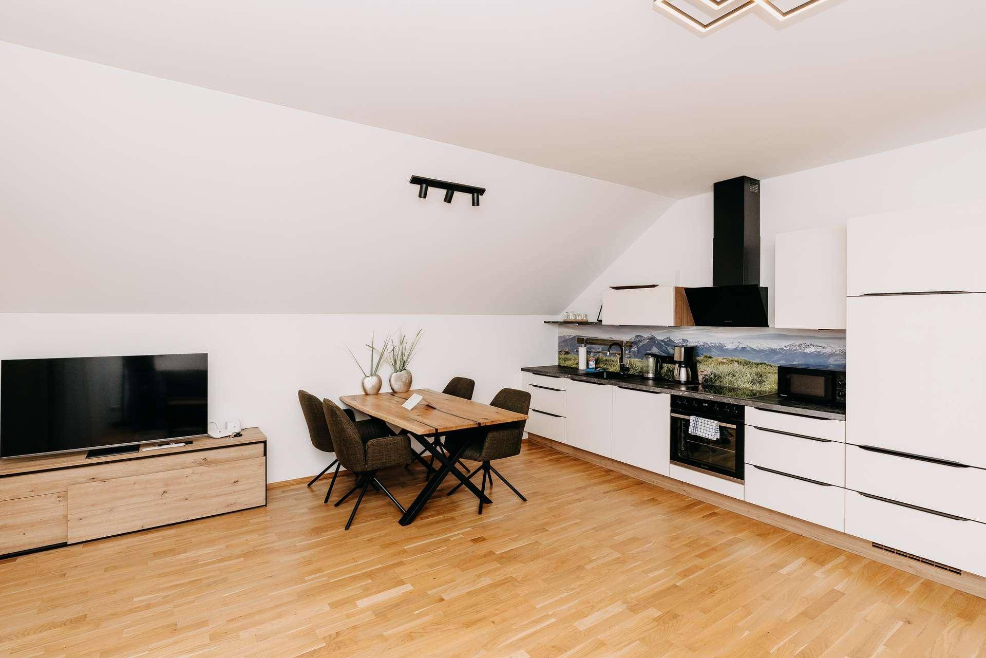 Moderne Einbauküche mit weißen Fronten, Essbereich und Blick auf die Berglandschaft.