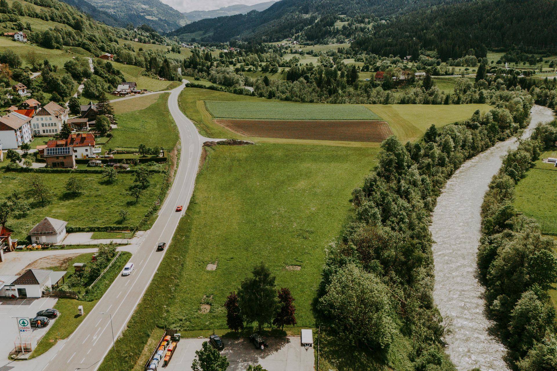 Panoramablick aus der Vogelperspektive auf eine Flusslandschaft mit Straße, grünen Feldern und Häusern im Tal.