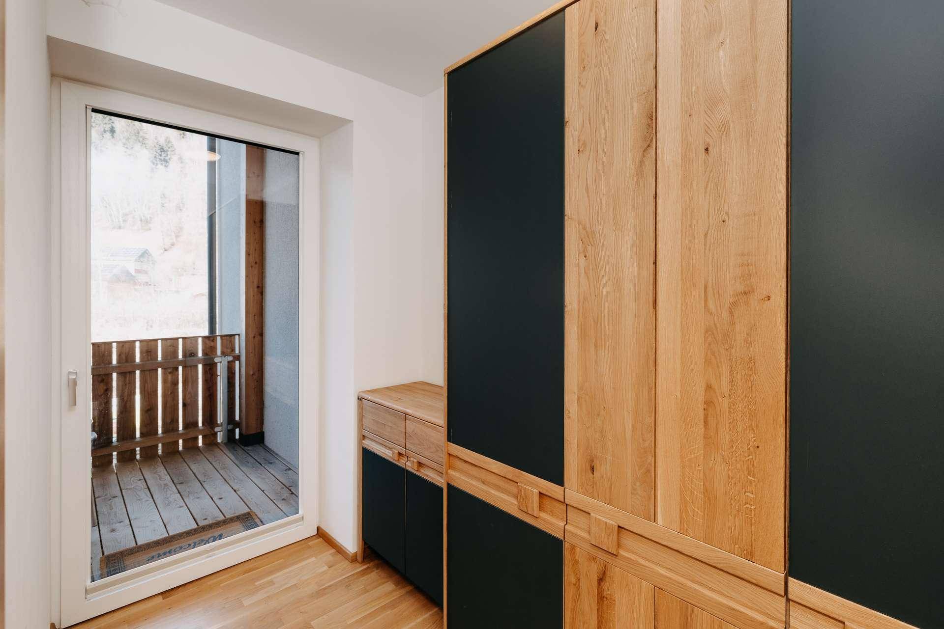 Moderner Kleiderschrank aus Holz und dunklen Elementen neben einem Balkonzugang.