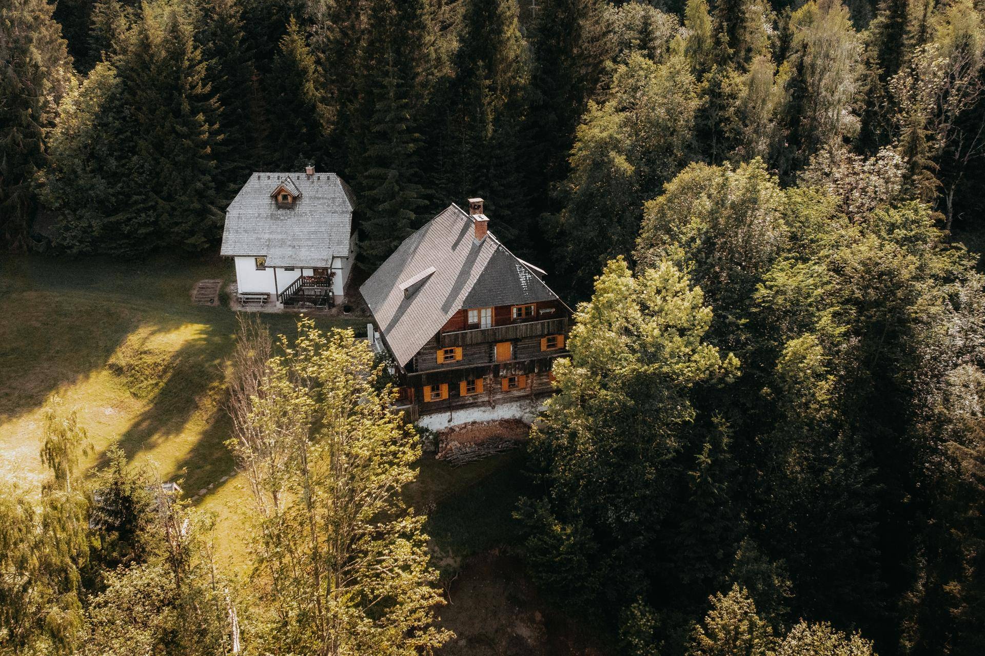 Luftaufnahme von zwei traditionellen Häusern inmitten eines bewaldeten Berghangs.