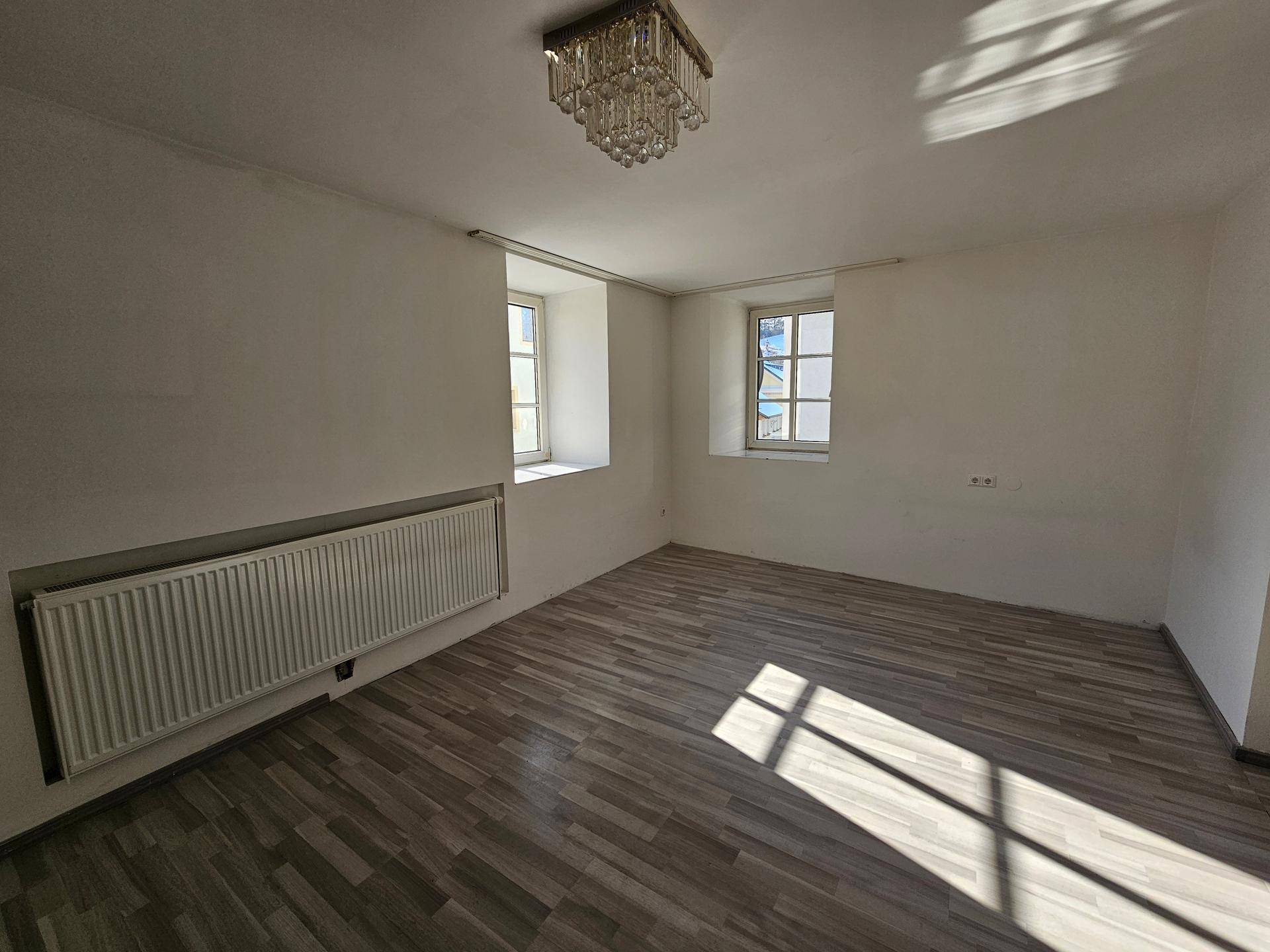 Heller Raum mit Laminatboden, zwei Fenstern und einem Heizkörper unterhalb der Fensterbank.