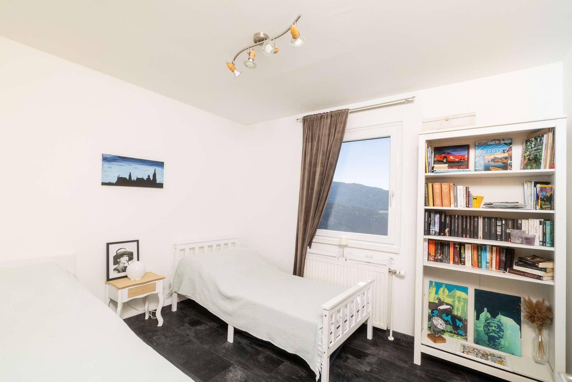 Schlafzimmer mit zwei Einzelbetten, Bücherregal und Fenster mit Blick ins Grüne.