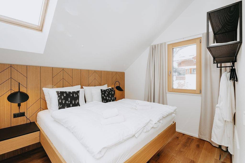 Schlafzimmer mit Holzboden, großem Fenster und modernem Dekor in heller Farbgebung.