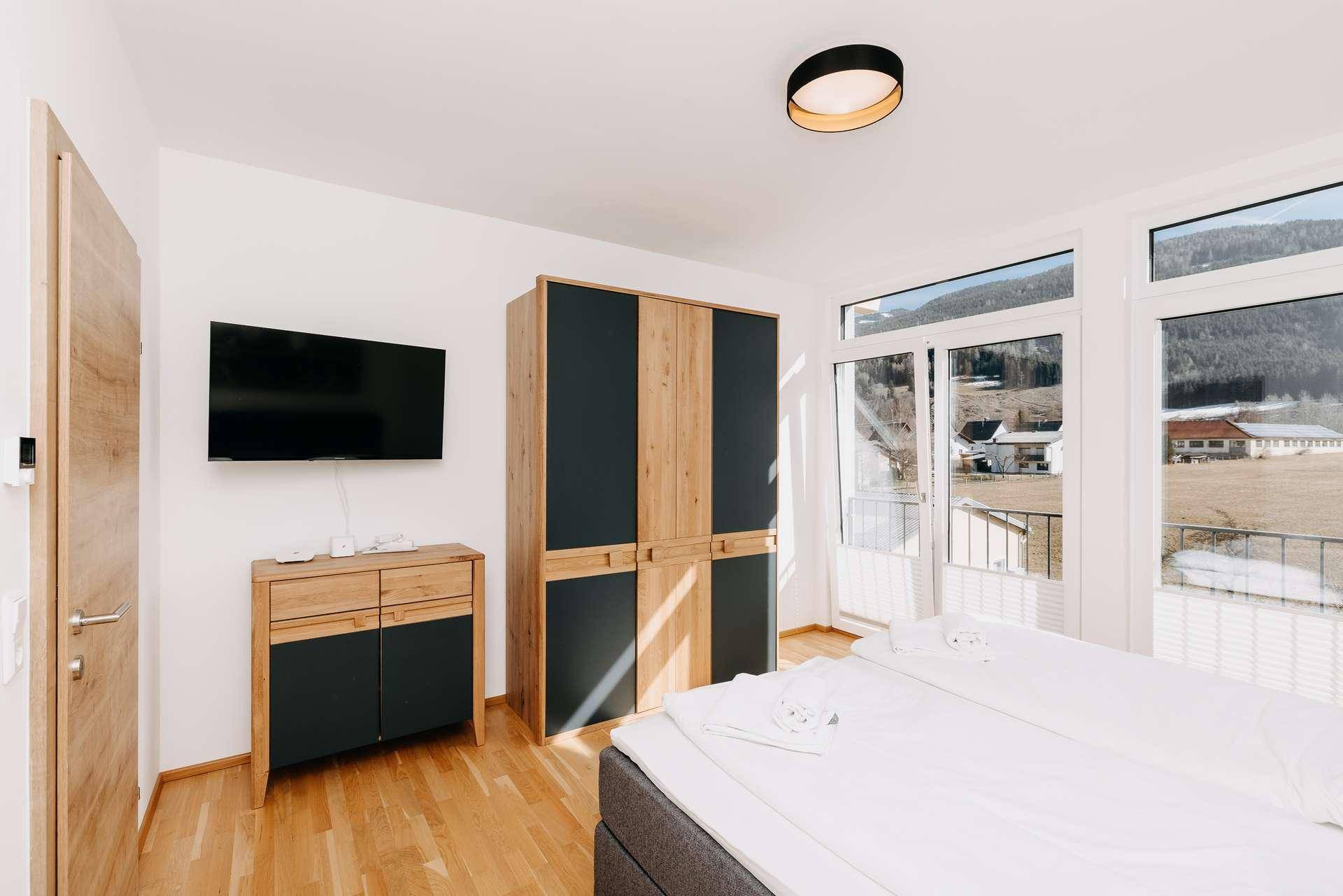 Modernes Schlafzimmer mit Holzboden, Kleiderschrank und Fernseher an der Wand.