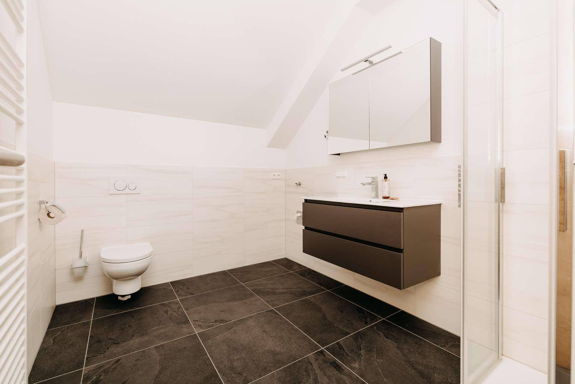 Modernes Badezimmer mit Dusche, wandhängendem WC, Einzelwaschbecken und dunklen Fliesen.