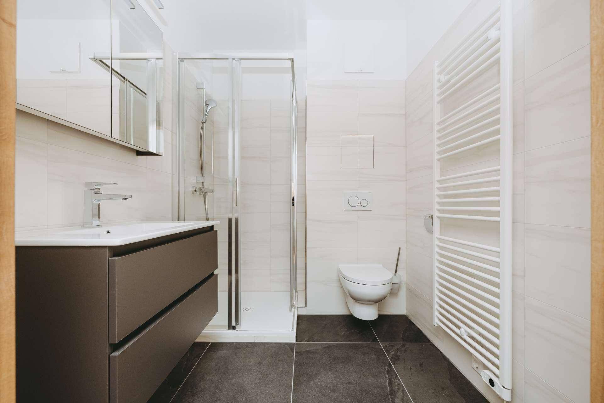 Modernes Badezimmer mit Dusche, Wand-WC, Einzelwaschbecken und beheiztem Handtuchhalter.