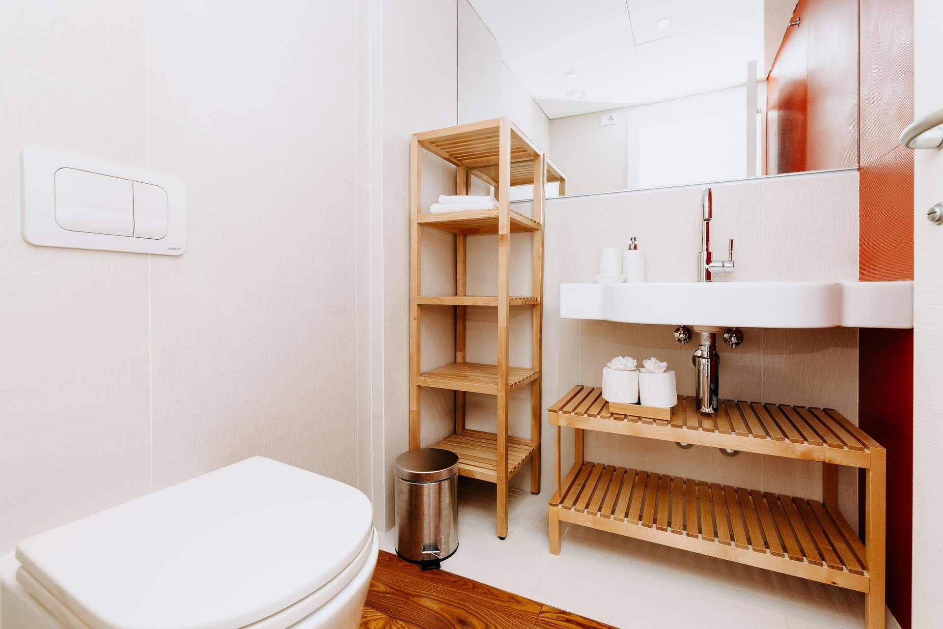 Modernes Gäste-WC mit weißer Keramik, Holzregalen und großem Spiegel.