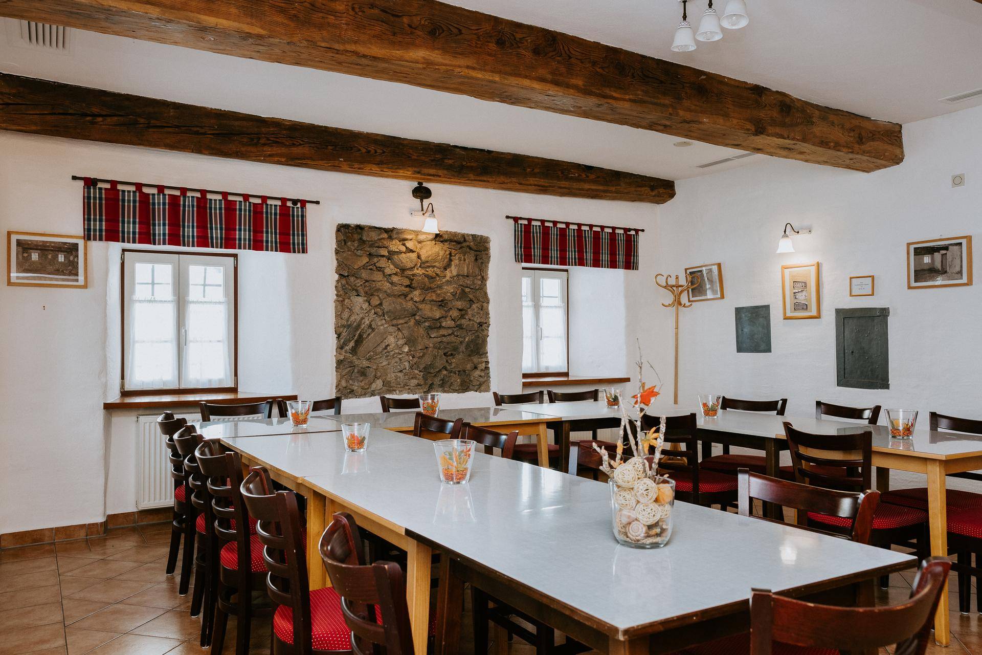 Großer Speisesaal mit Holzbalken, Steinelementen und mehreren Tischen für Veranstaltungen.