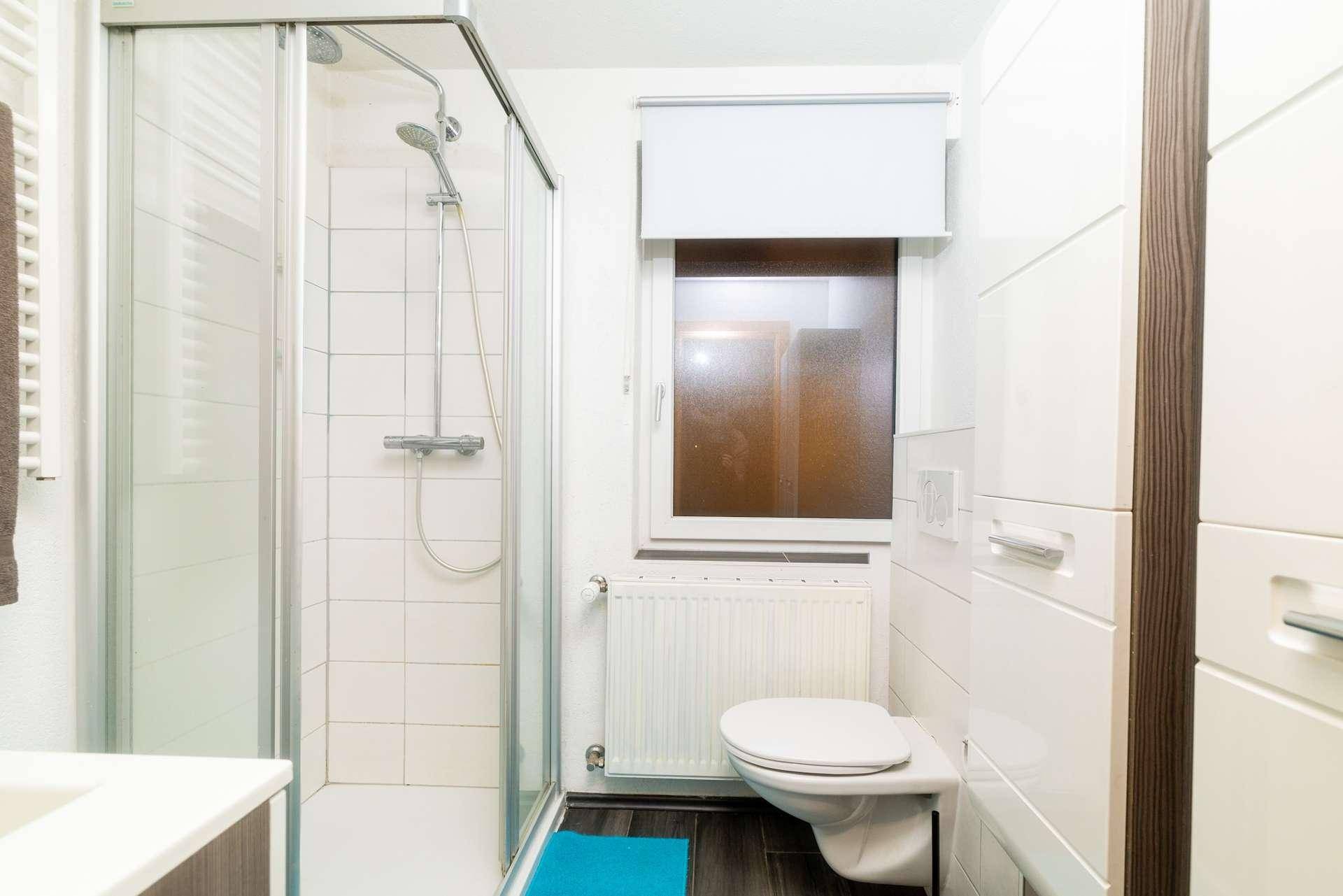 Kleines Badezimmer mit Duschkabine, wandhängendem WC und Fenster.