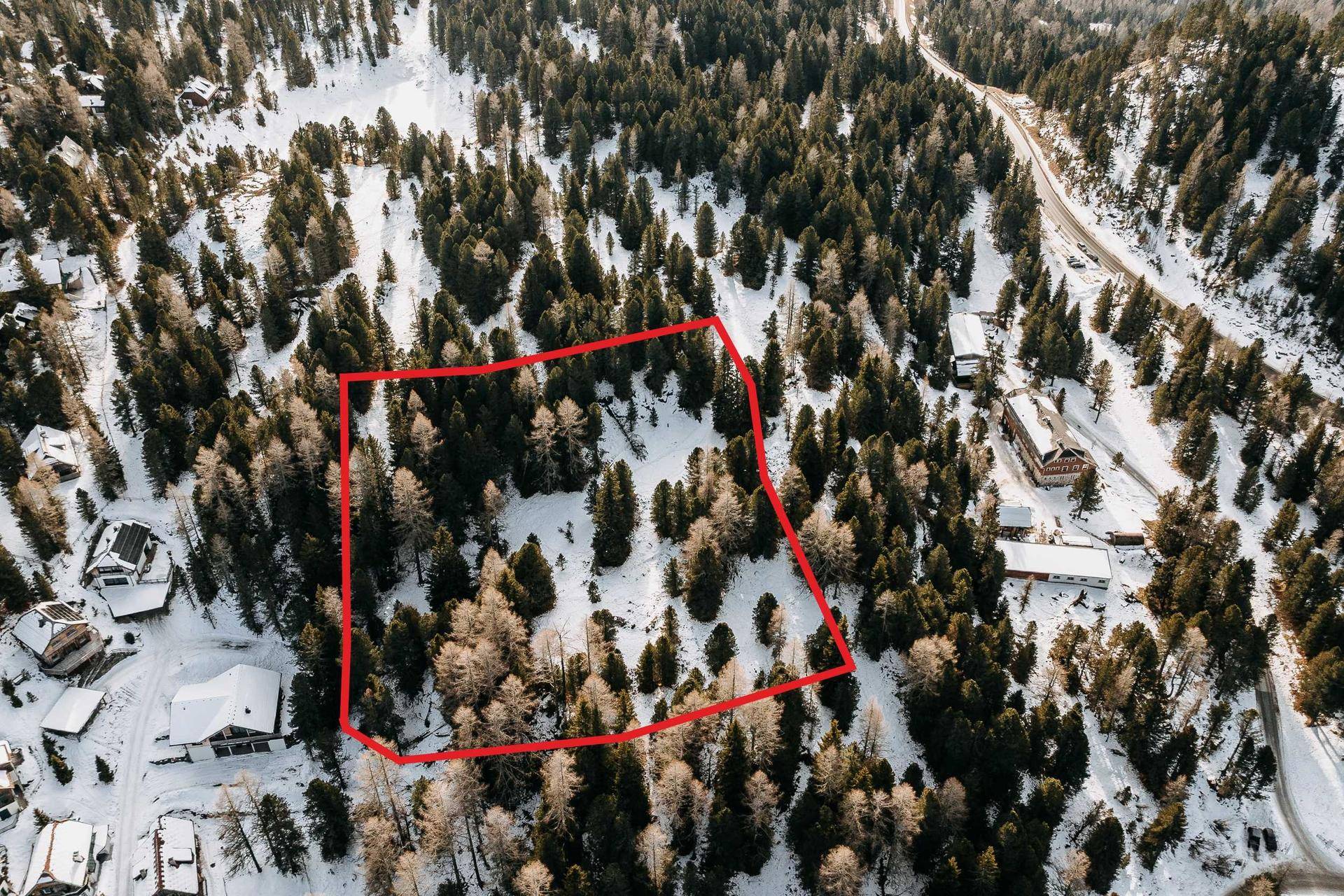 Luftaufnahme eines verschneiten Waldstücks mit einem rot markierten Grundstück in alpiner Umgebung.