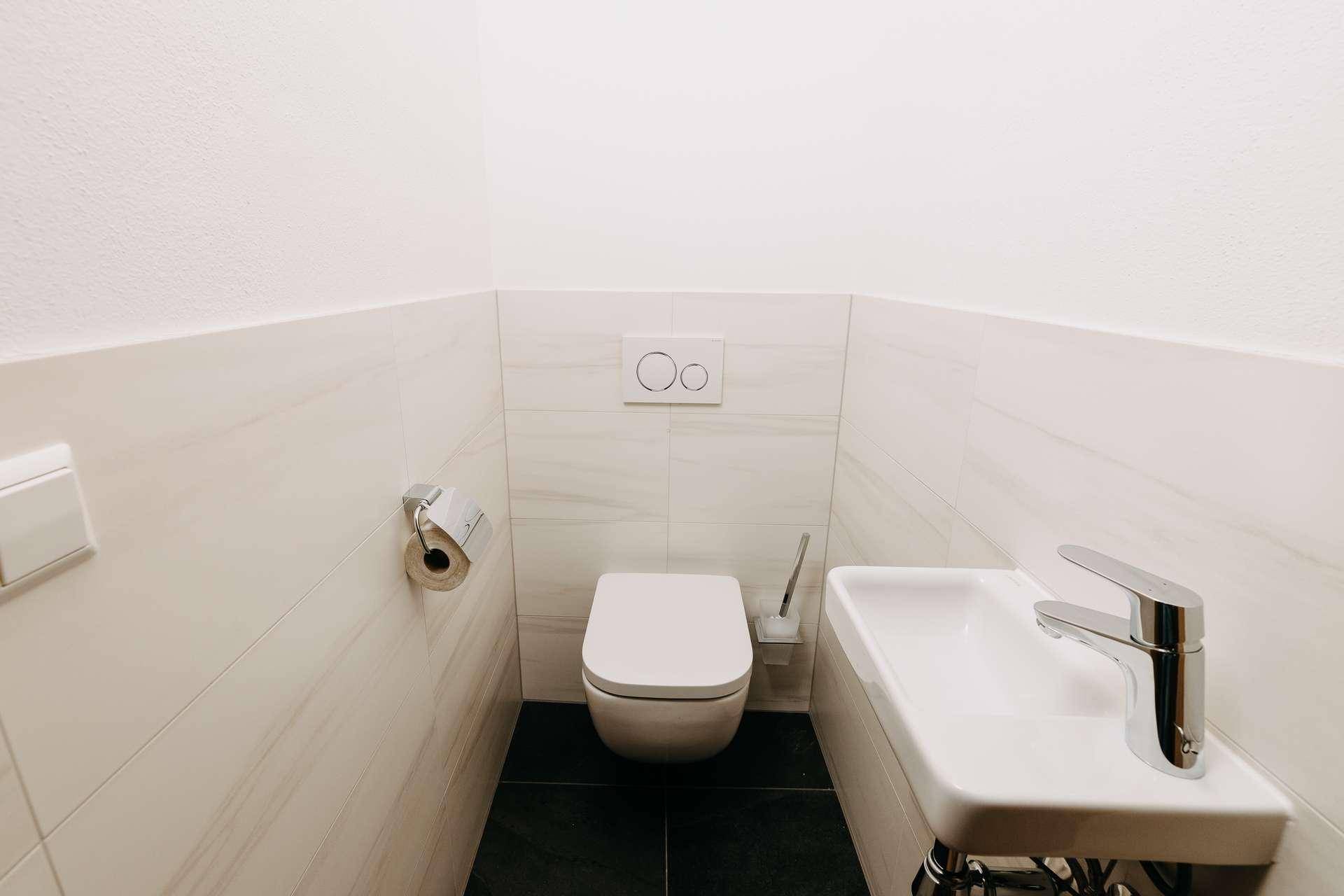 Modernes Gäste-WC mit wandhängender Toilette und kleinem Waschbecken.