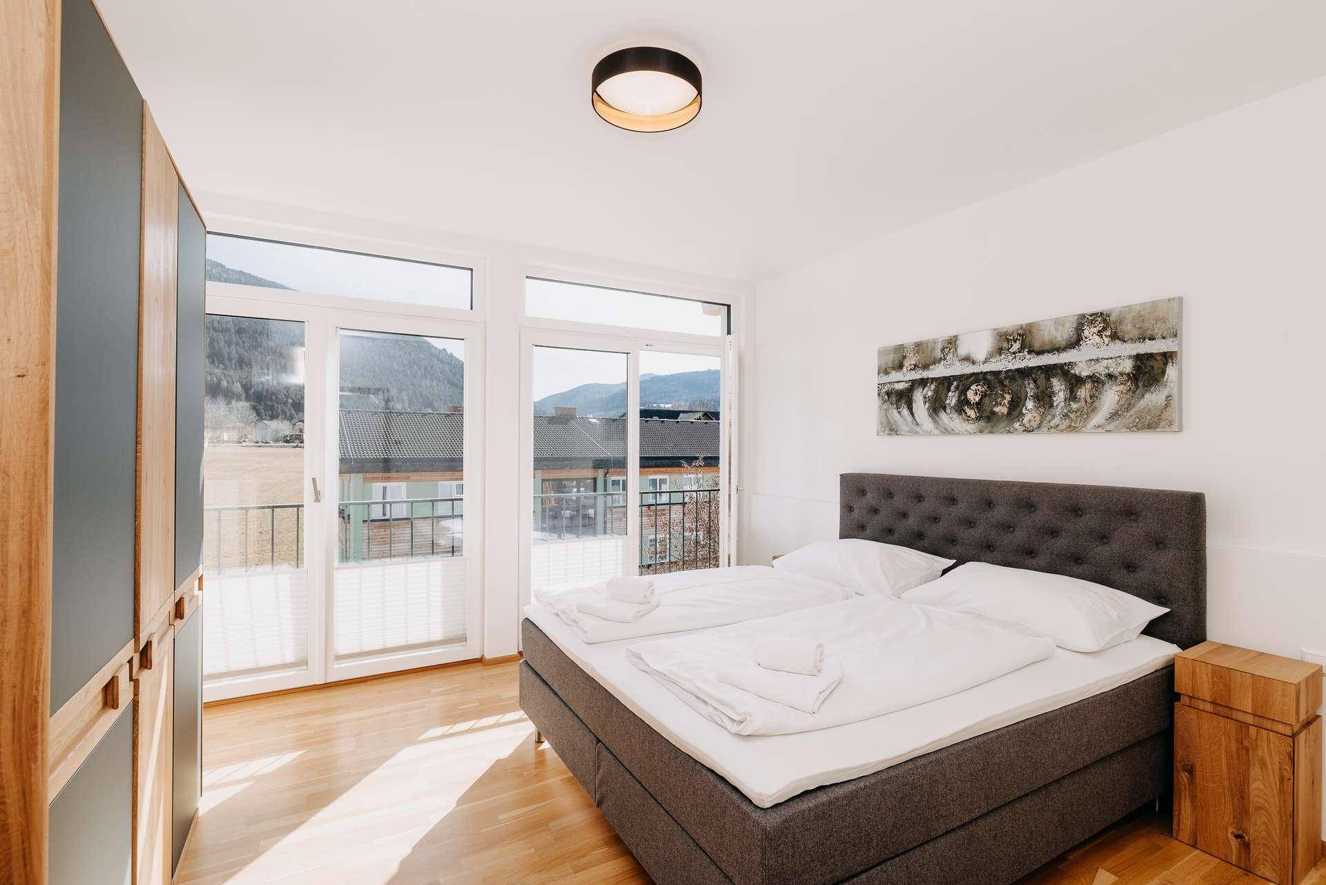 Helles Schlafzimmer mit Doppelbett, Holzboden und großen Fenstern mit Bergblick.