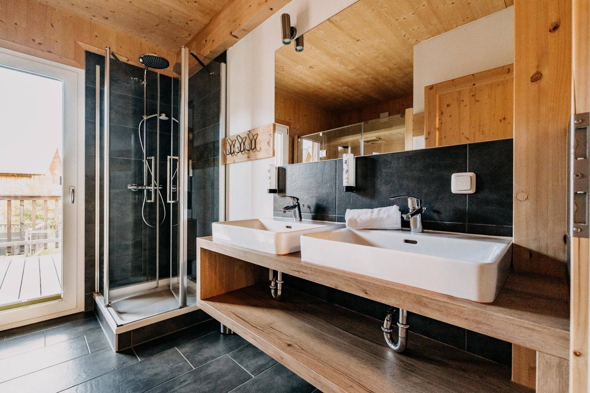 Modernes Badezimmer mit Doppelwaschbecken, großer Dusche und Holzelementen.