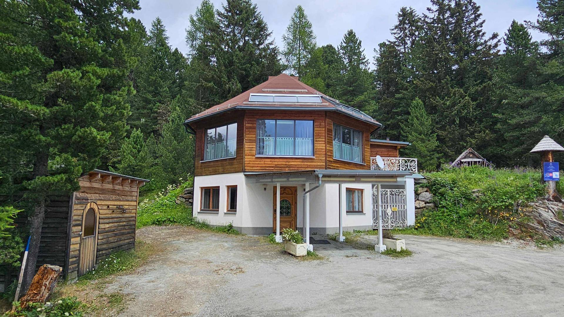 Modernes Holzhaus mit achteckigem Grundriss und großen Fensterfronten, eingebettet in eine grüne Waldlandschaft.