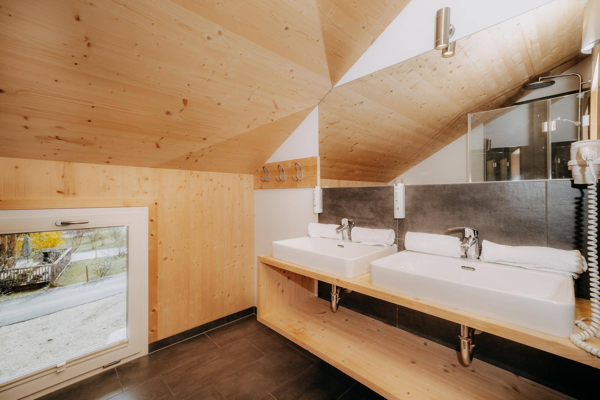 Modernes Badezimmer mit Doppelwaschbecken, Dusche und Holzwänden unter schräger Decke.