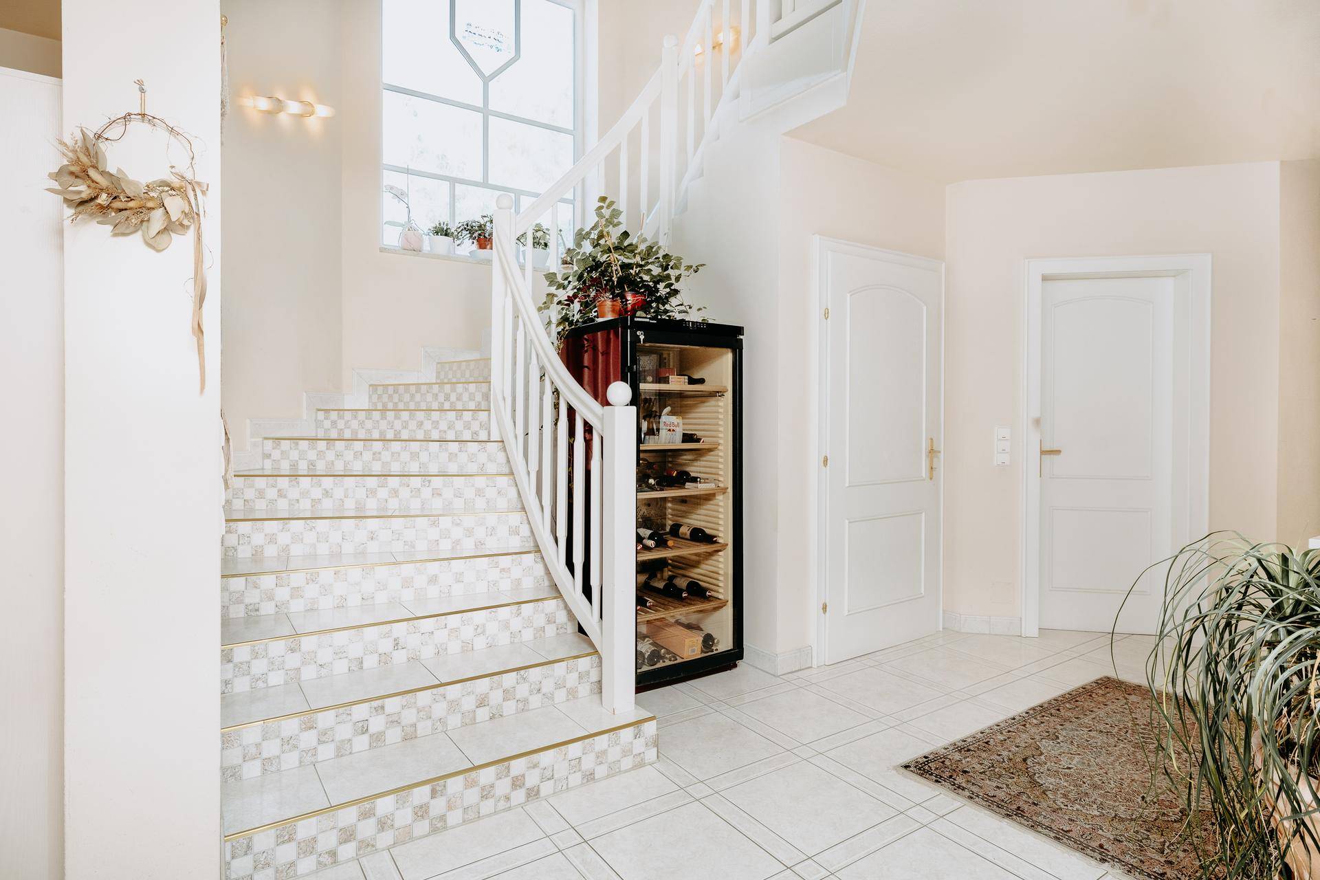 Elegantes Treppenhaus mit geschwungener Treppe, Fliesenboden und integriertem Weinkühlschrank.