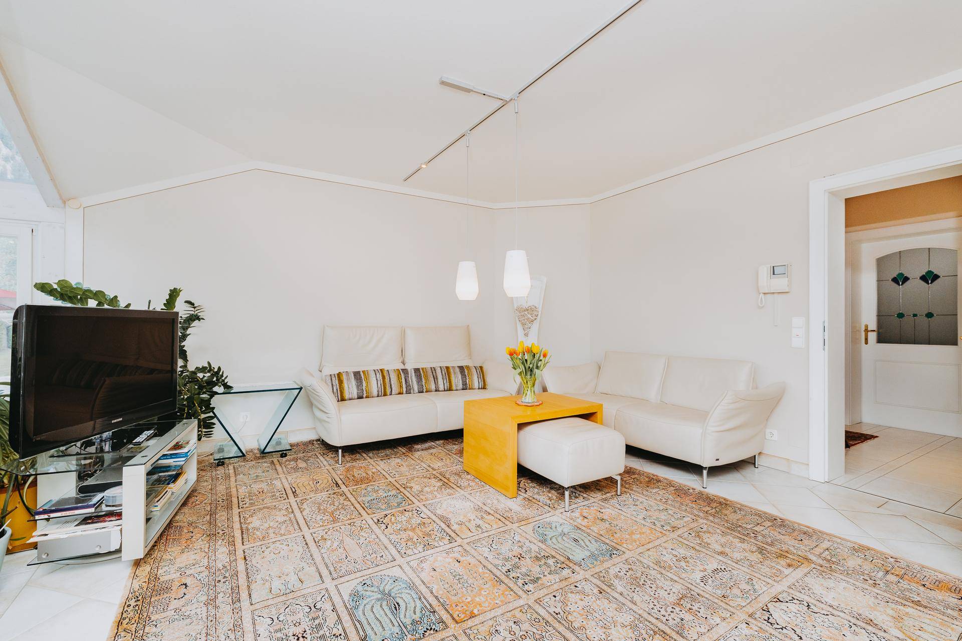 Helles Wohnzimmer mit beigen Sofas, Teppich und Blick in den Wintergarten.