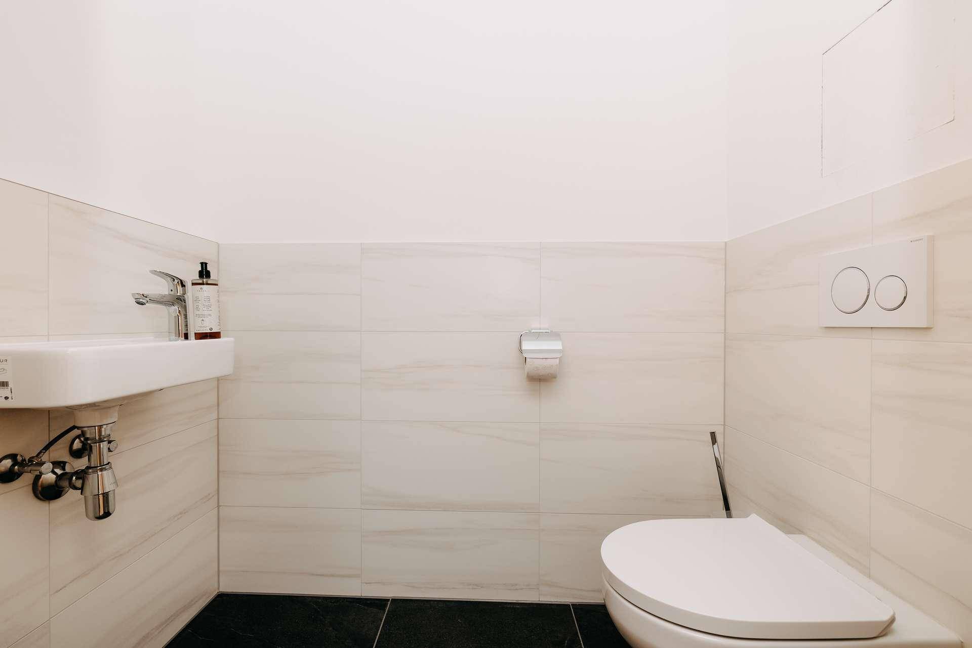 Kleines Gäste-WC mit wandhängendem WC und Handwaschbecken, ausgestattet mit dunklen Fliesen.