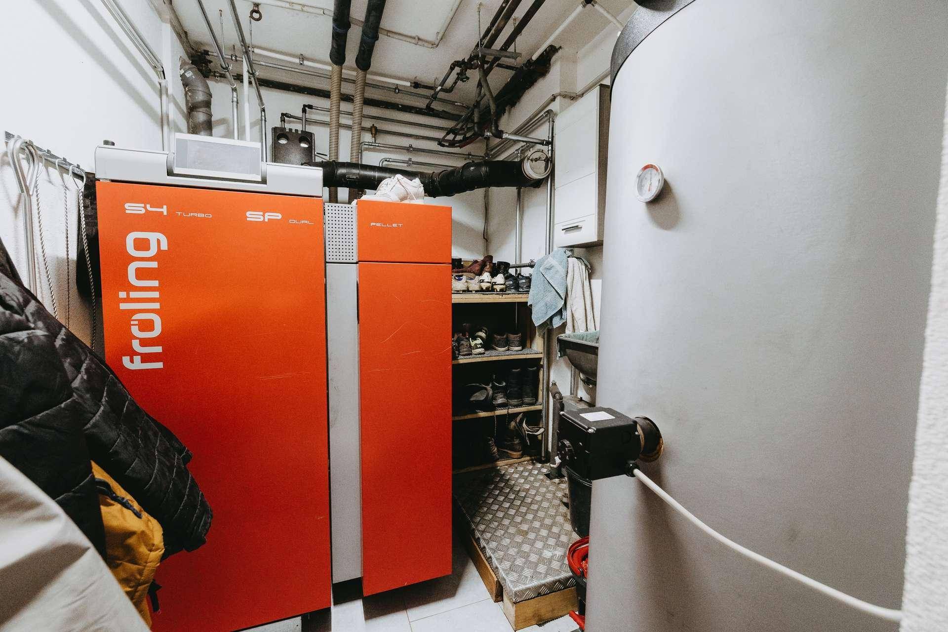 Heizungsraum mit moderner Pelletheizung, Warmwasserspeicher und sichtbaren Rohren an der Decke.