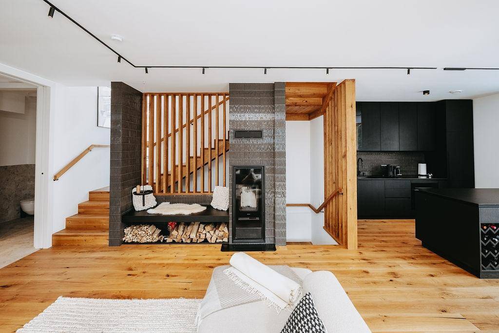 Offener Wohnbereich mit Holzboden, Treppe und moderner schwarzer Küche im Hintergrund.